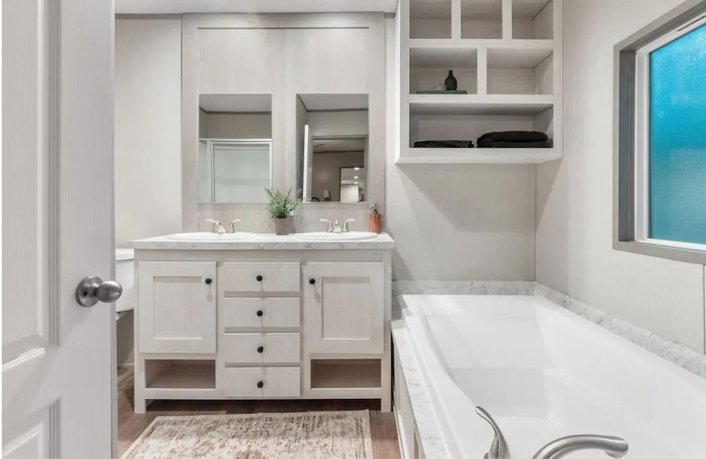 Modern bathroom with double sinks, white cabinetry, built-in shelving, a large bathtub, and frosted window, featuring neutral tones and minimal decor.