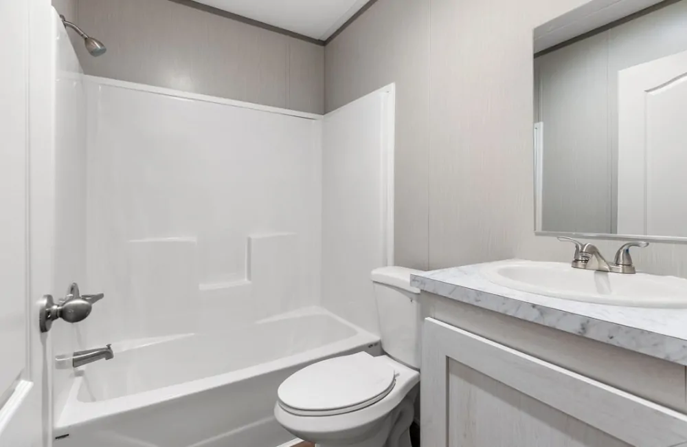 A clean, simple bathroom with a white bathtub-shower combination, toilet, and a sink with a marble countertop and mirrored cabinet above.
