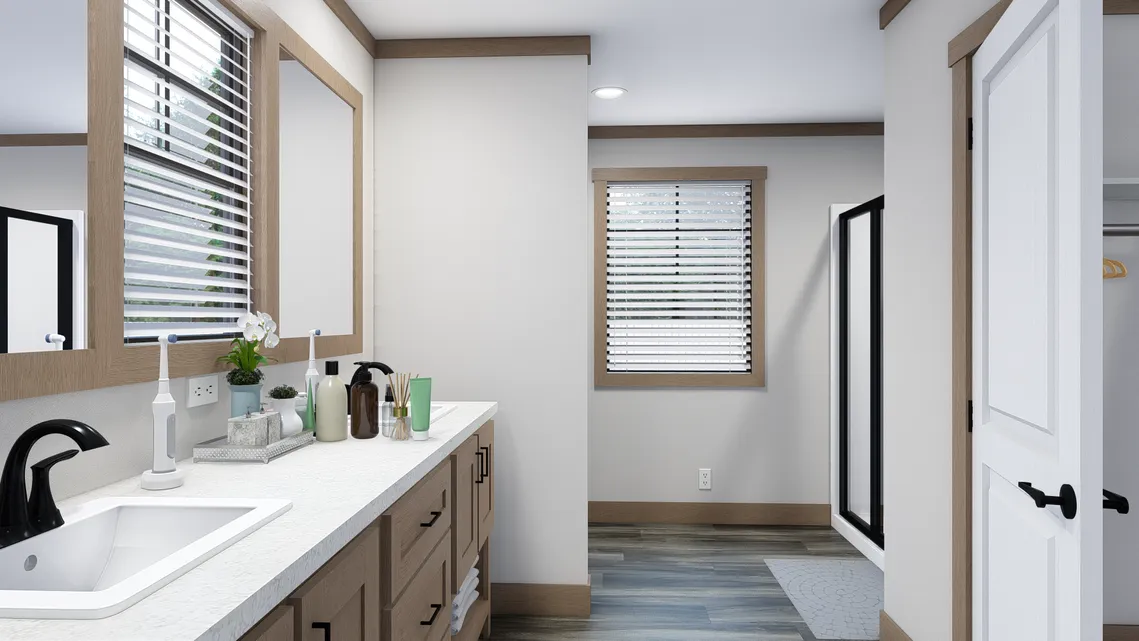 Modern bathroom with a large vanity, sink, assorted toiletries, mirrors, window blinds, and a walk-in shower in the background.
