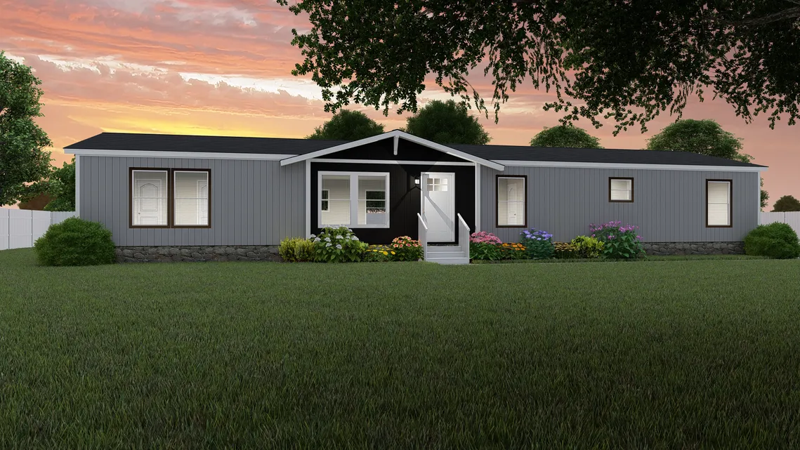 A modern gray manufactured home with white trim, a small porch, landscaped flowers in front, and a large lawn, set against a sunset sky.