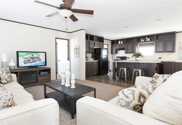 Modern living room with beige sofas, a coffee table with candle holders, a television, and an open kitchen with dark cabinets in the background.