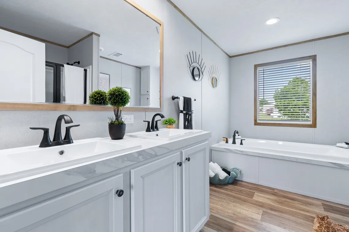 Modern bathroom with double sinks, black fixtures, a large mirror, a bathtub, wood-look flooring, and a window with blinds letting in natural light.