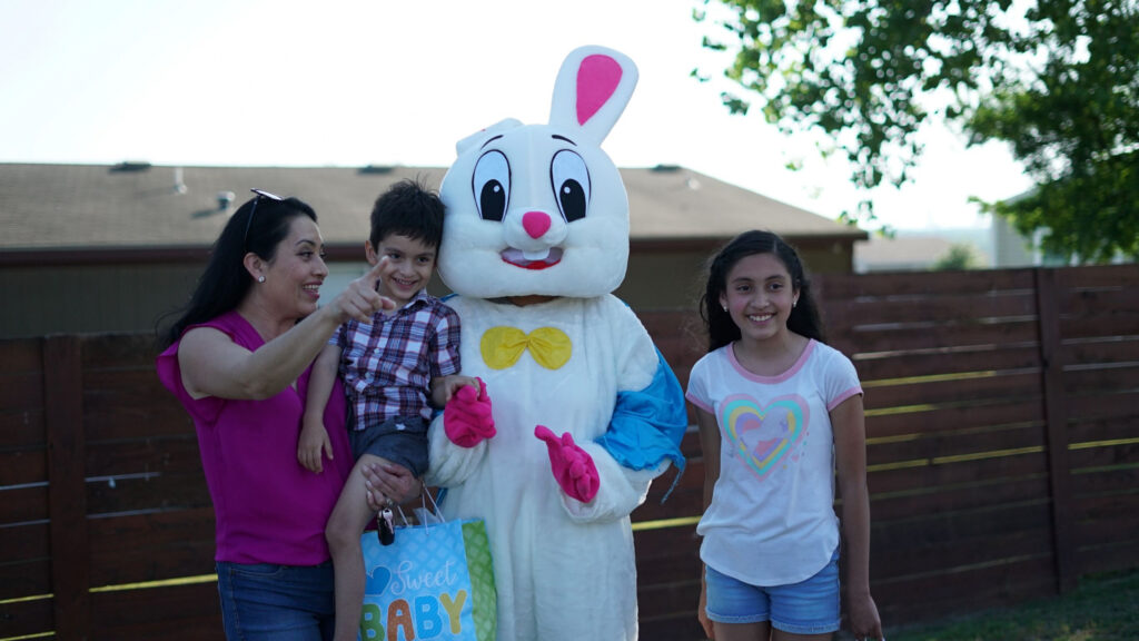 A woman, two children, and a person in a bunny costume pose for a photo outdoors in front of a wooden fence.