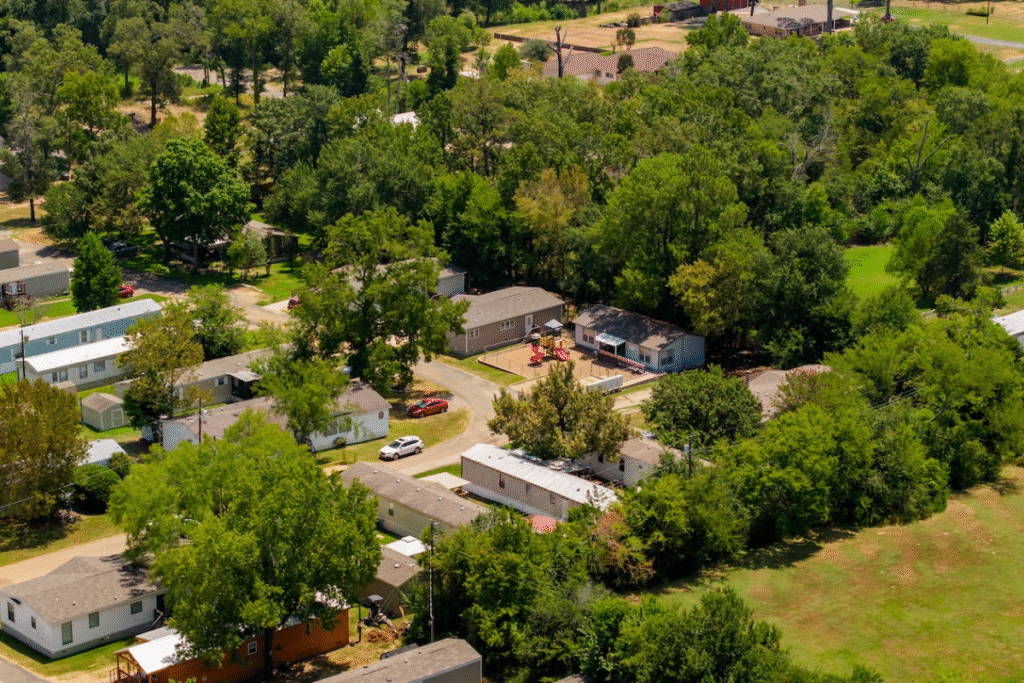 Aerial view of a residential neighborhood with houses, trees, parked cars, and green lawns under sunlight.