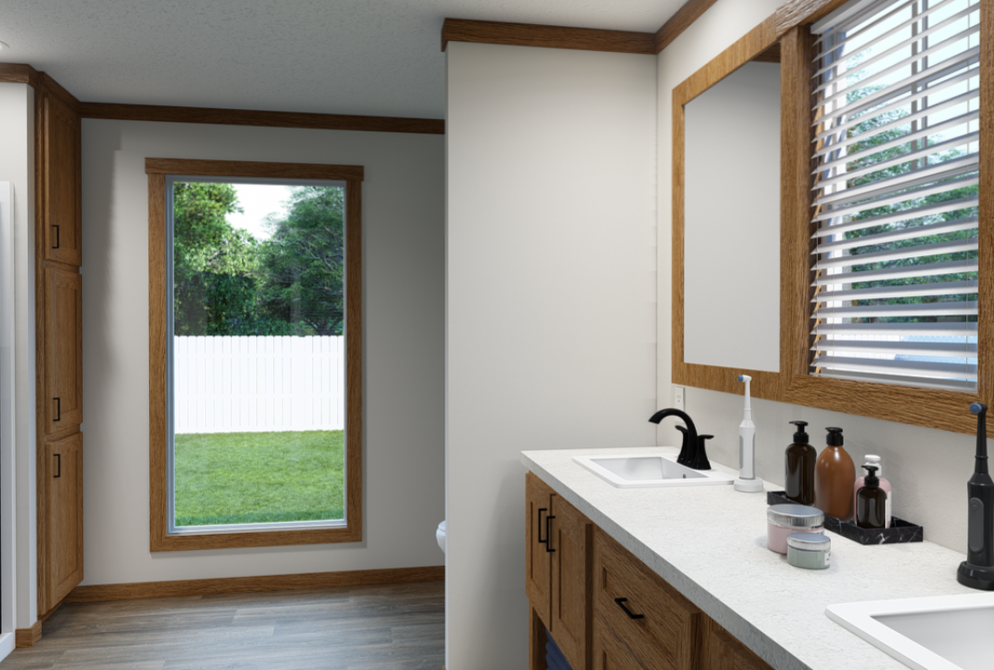 A bathroom with a double sink vanity, countertop items, wood-framed mirror, and a window showing a green yard with a white fence.