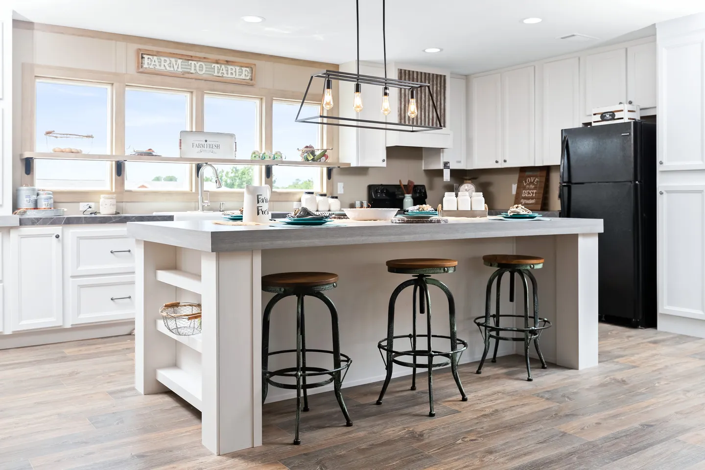 Modern farmhouse kitchen with white cabinets, a large island with three barstools, open shelving, pendant lights, and a black refrigerator.