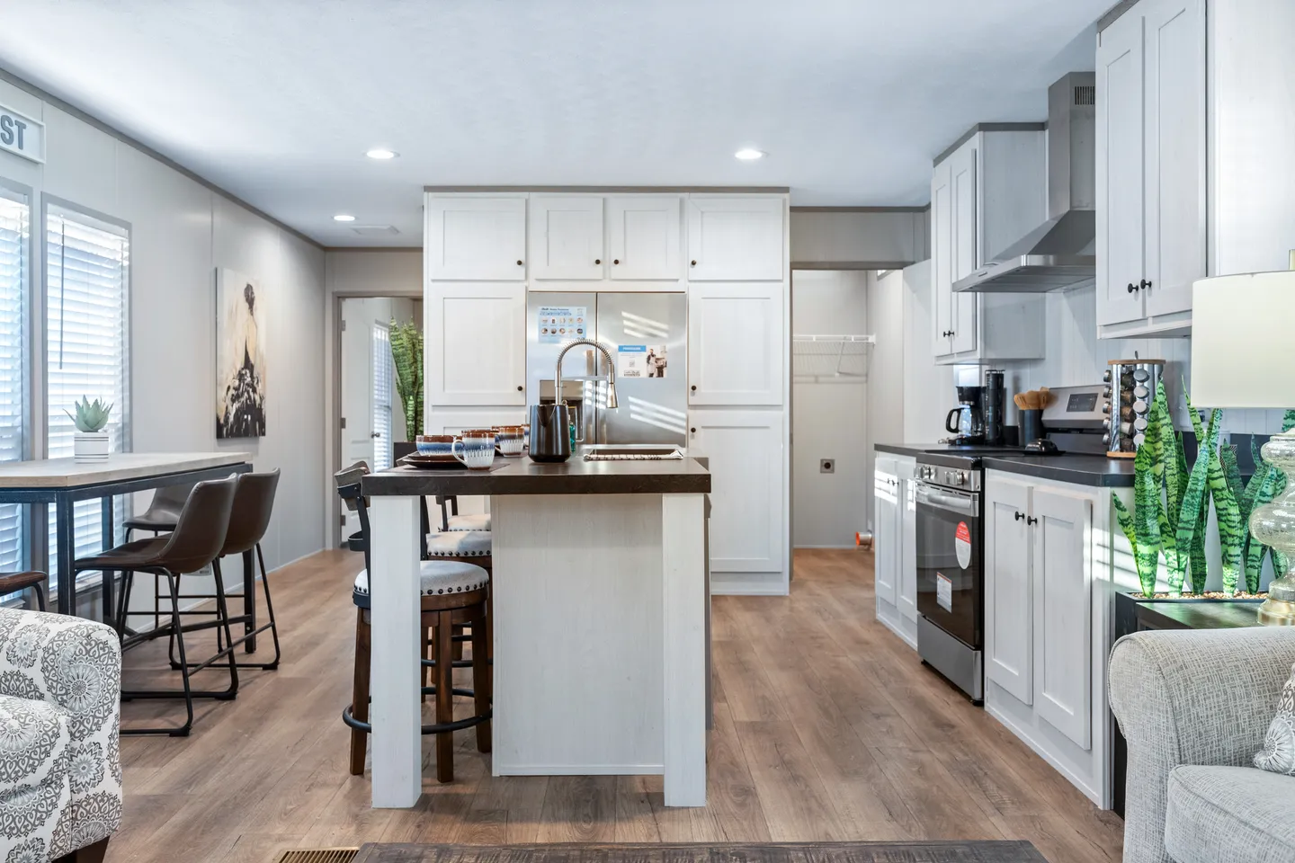 Modern kitchen with white cabinets, stainless steel appliances, a center island with stools, and wood flooring, connected to a dining area and living space.