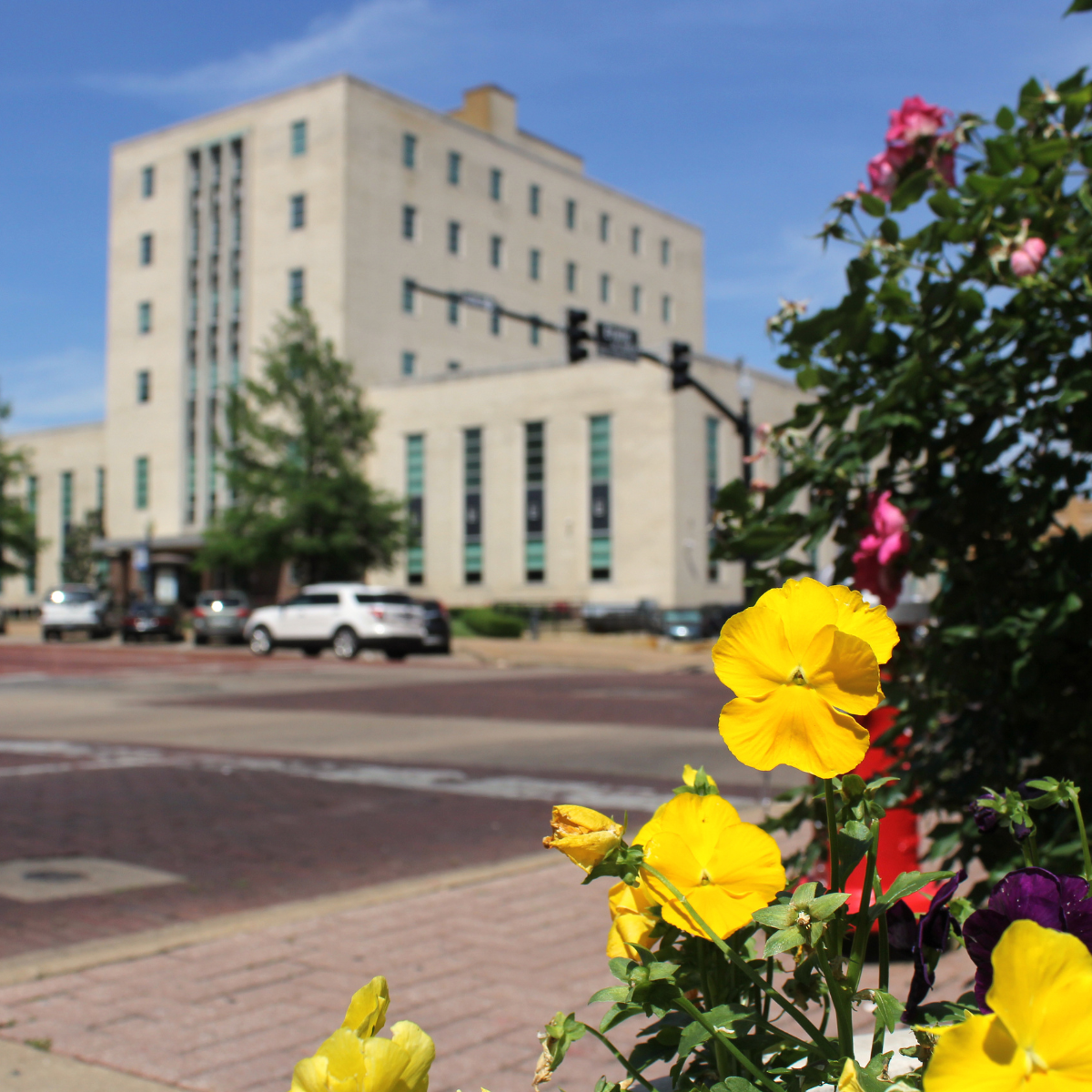 Modern bathroom with a freestanding bathtub, double sinks, large mirrors, and wood accents. Blinds cover the windows and various toiletries are on the countertop.
