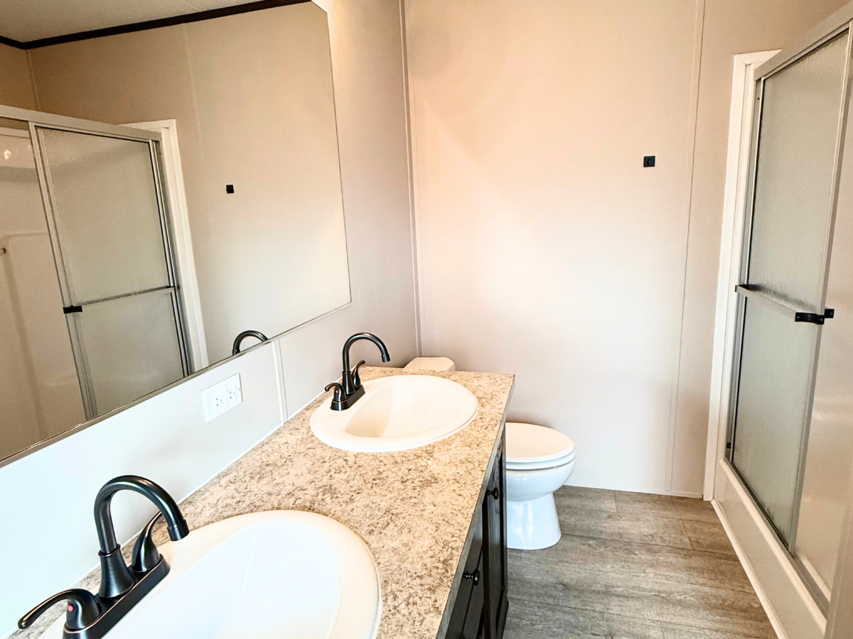 Modern bathroom with a double sink vanity, marble countertop, large mirror, toilet, and glass-enclosed shower.