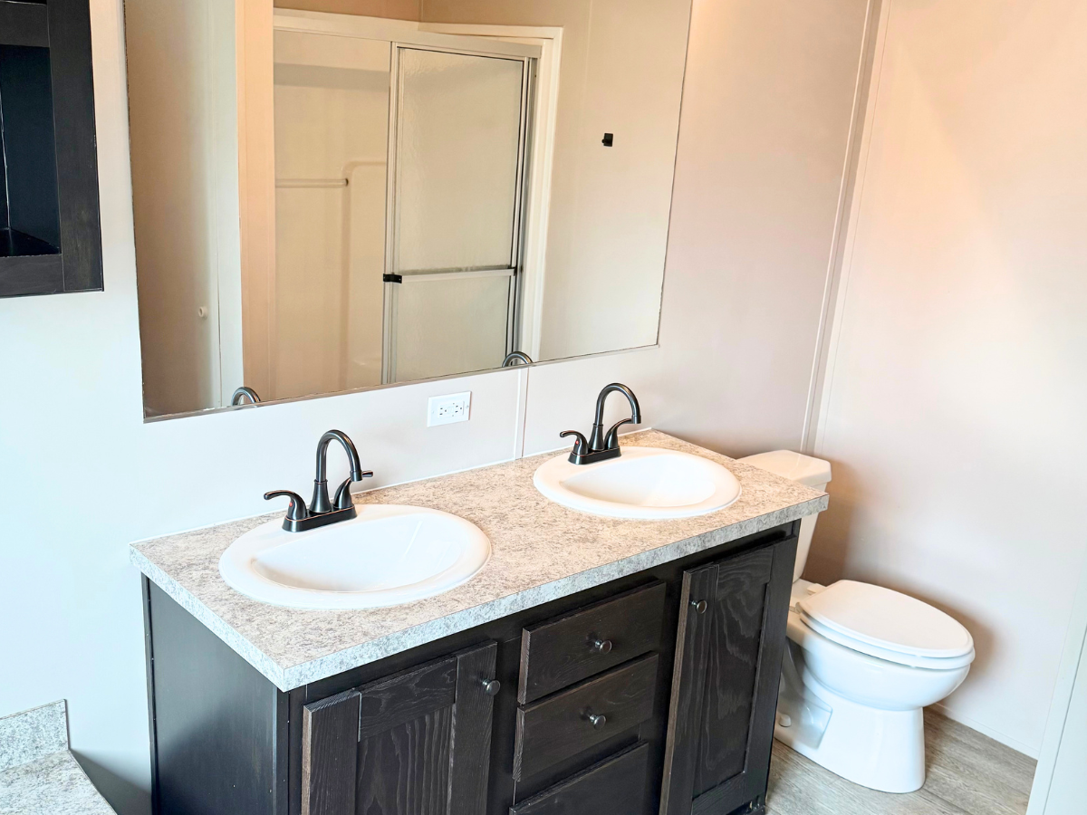 Modern bathroom with a double sink vanity, large mirror, toilet, and a glass-enclosed shower in the background.
