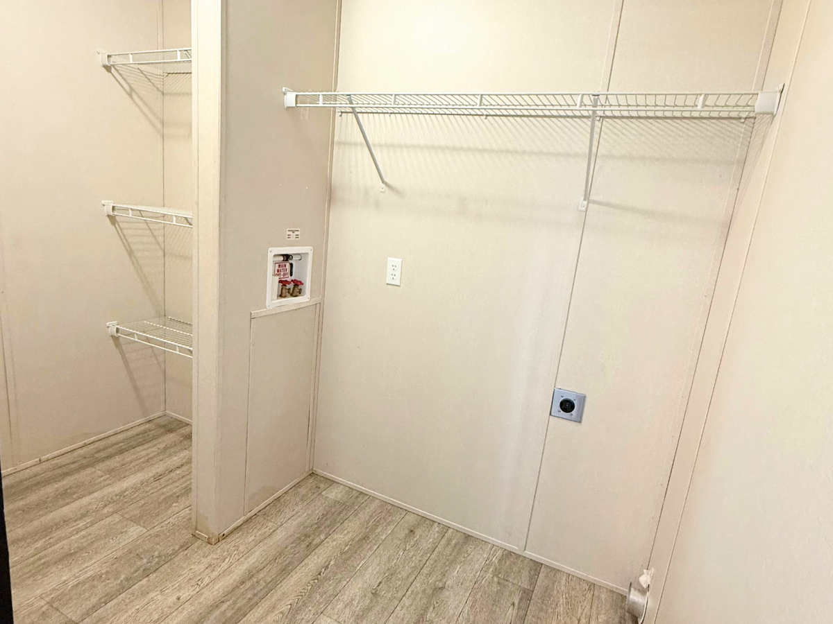 Empty laundry room with beige walls, light wood flooring, white wire shelves, and hookups for a washer and dryer.