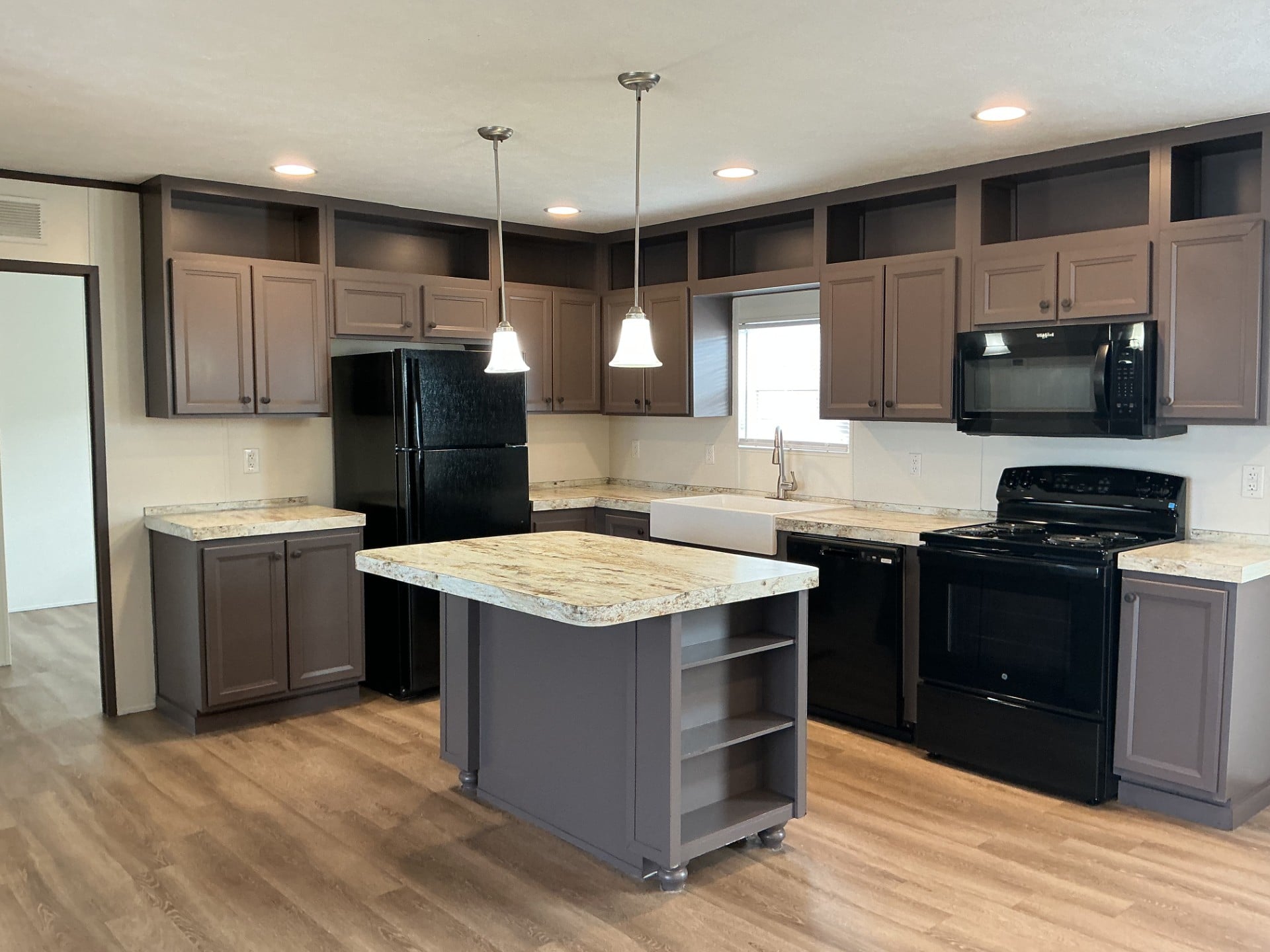 Modern kitchen with brown cabinets, black appliances, granite countertops, an island with shelves, pendant lights, and wood flooring.