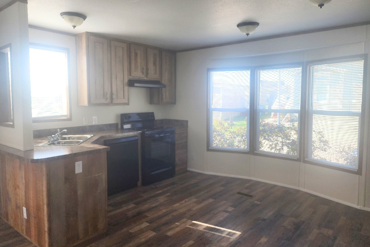 Kitchen with wood cabinets, dark appliances, and corner sink. Large windows with blinds let in natural light. Wood-patterned flooring throughout.