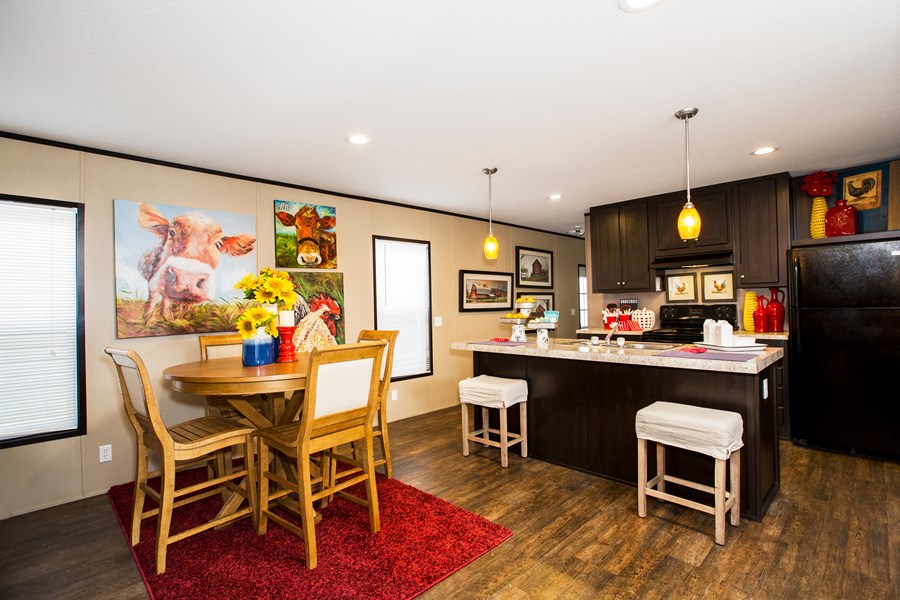 A kitchen with dark cabinets, a black refrigerator, an island with stools, a round dining table with chairs, colorful decor, and cow-themed artwork on the walls.