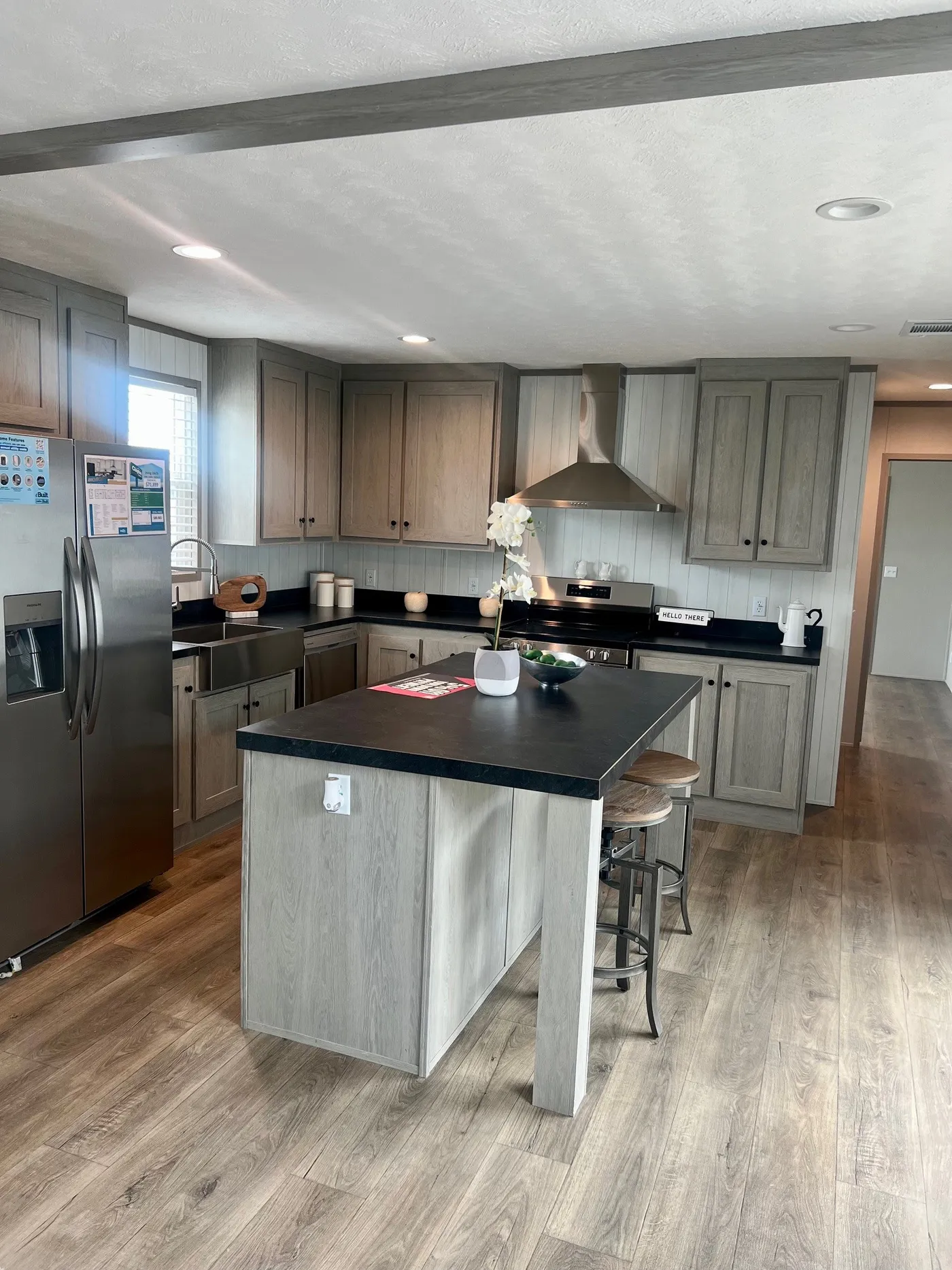 Modern kitchen with stainless steel appliances, light gray wood cabinets, black countertops, and a small island with stools and a white orchid centerpiece.