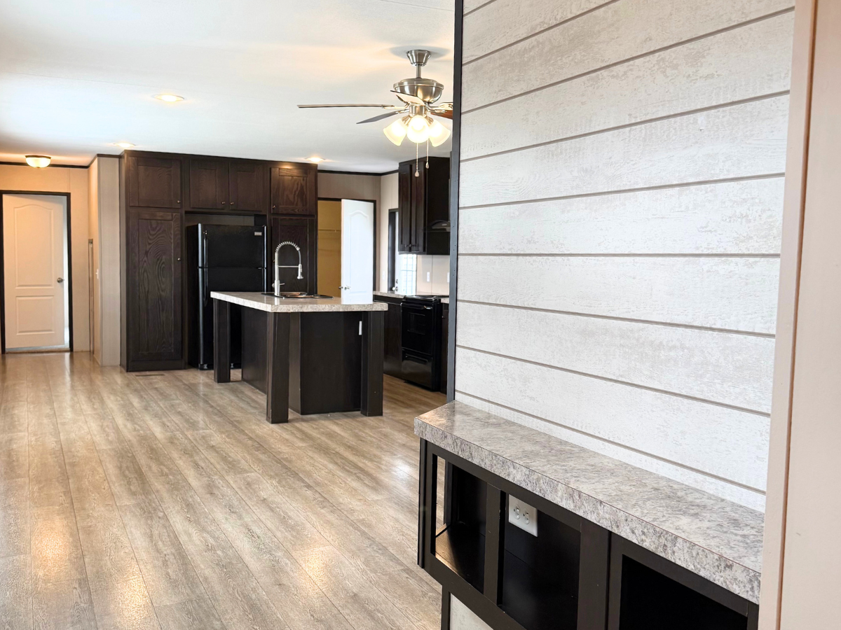 Modern kitchen with dark cabinets, center island, wood-look flooring, ceiling fan with lights, and a built-in shelf against a white shiplap accent wall.