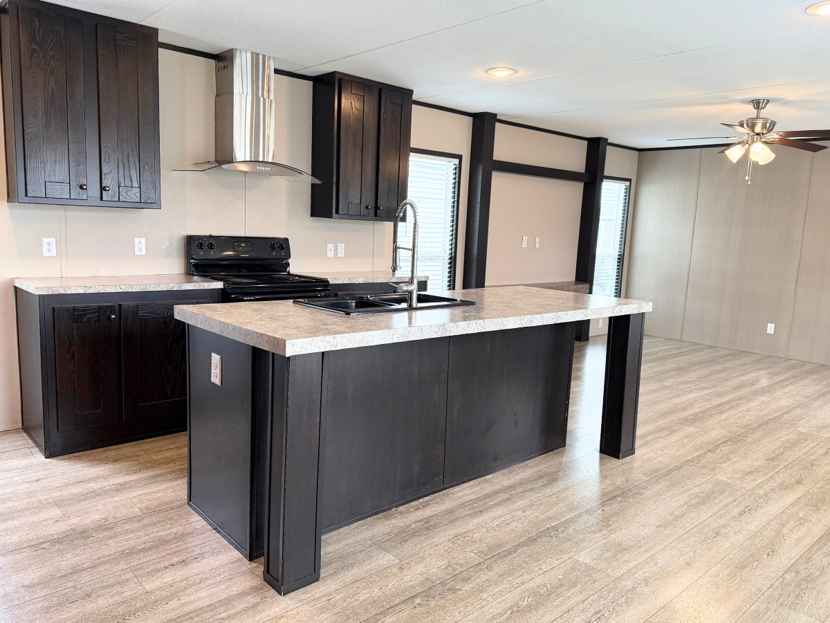Modern kitchen with dark wood cabinets, a center island with sink, electric stove, range hood, light wood floors, and an adjacent open area with a ceiling fan.