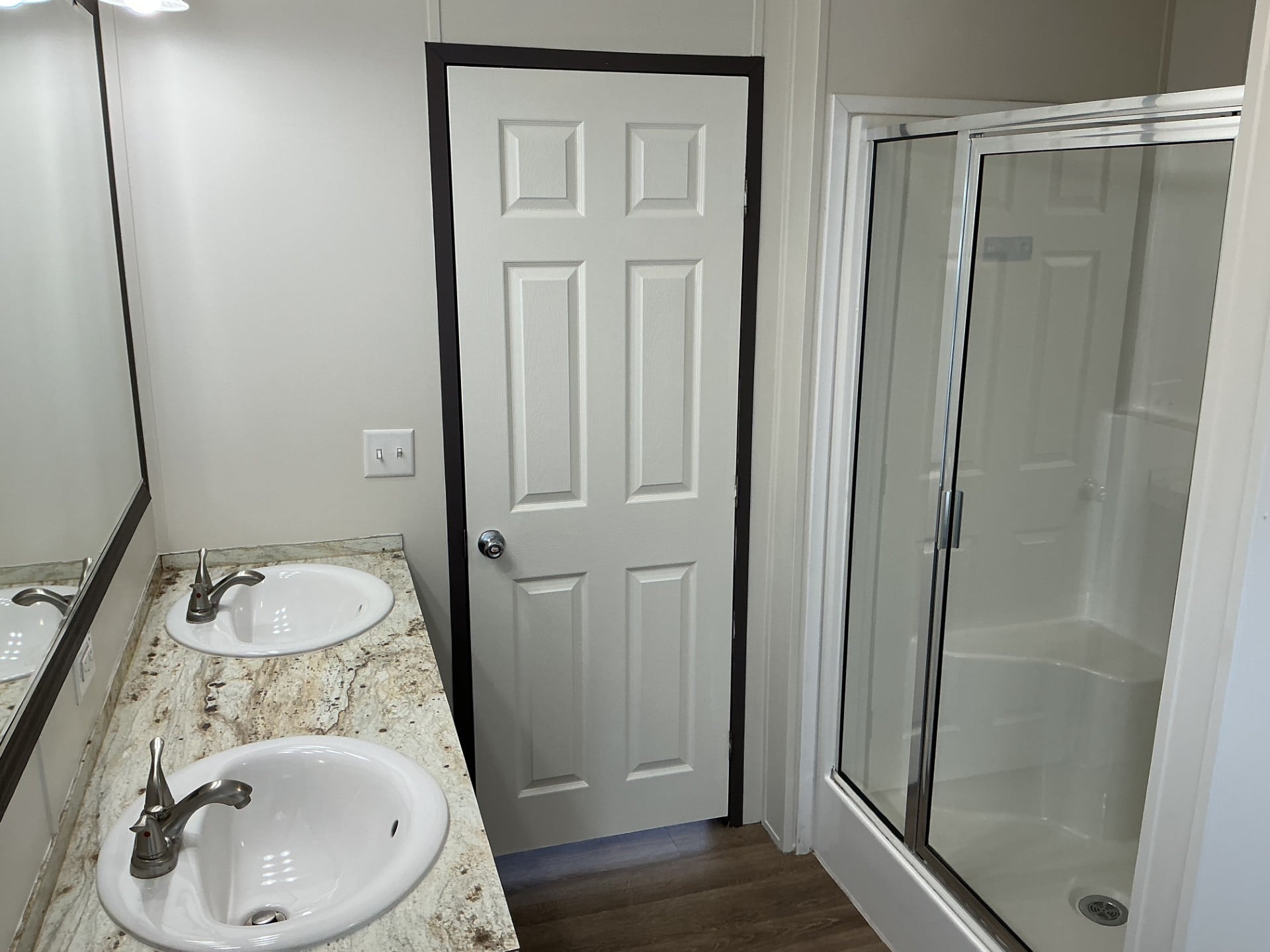 A bathroom with a double sink vanity, a door in the center, and a glass-enclosed shower on the right.