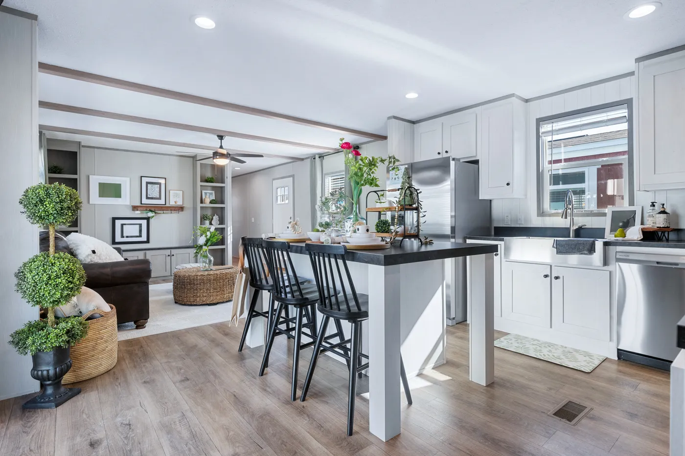 Modern open-concept kitchen and living area with white cabinetry, black accents, island seating, stainless steel appliances, and wood flooring.