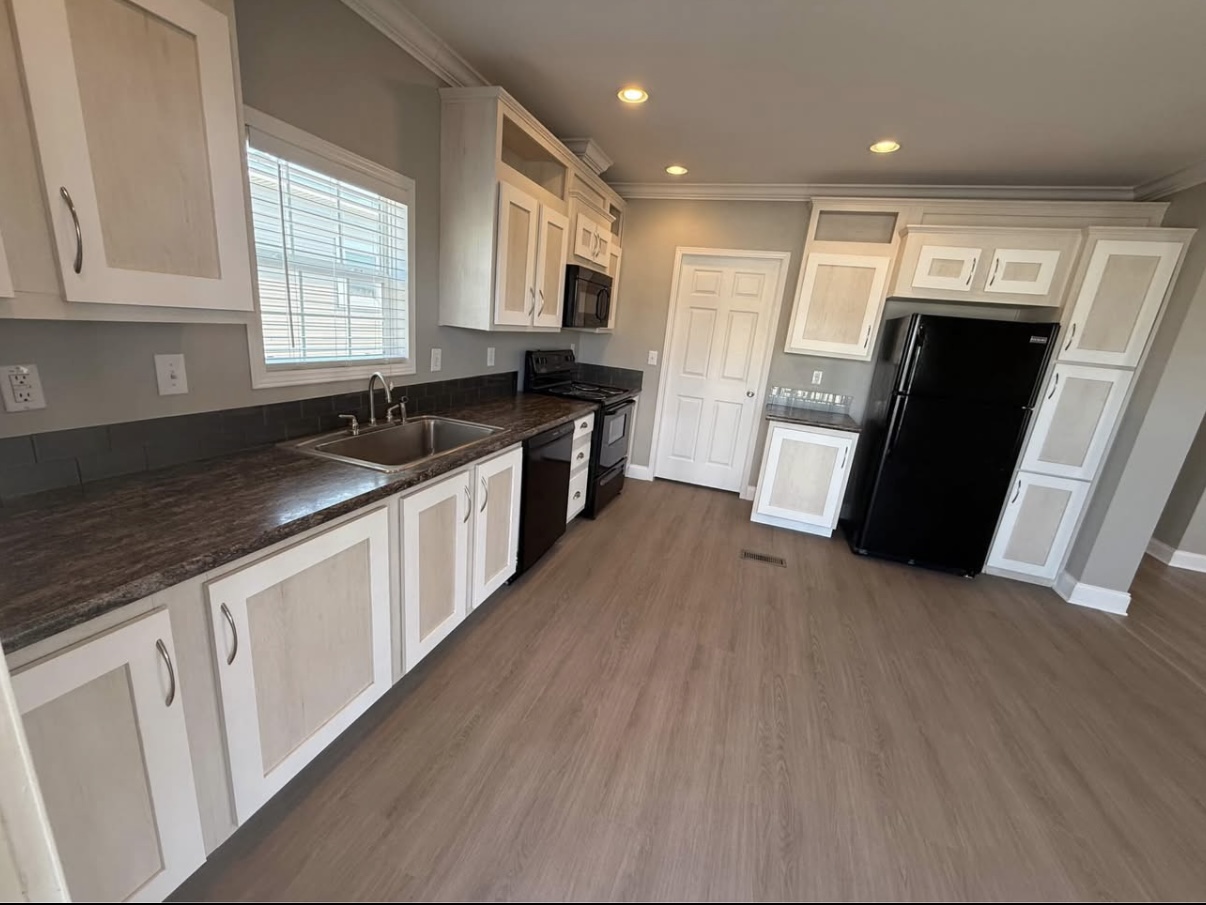 Modern kitchen with white cabinets, black appliances, a double sink, wood flooring, and a window above the countertop.