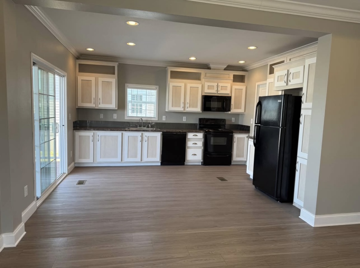 Modern kitchen with white cabinets, black appliances, wood-style flooring, recessed lighting, and large sliding glass doors on the left.