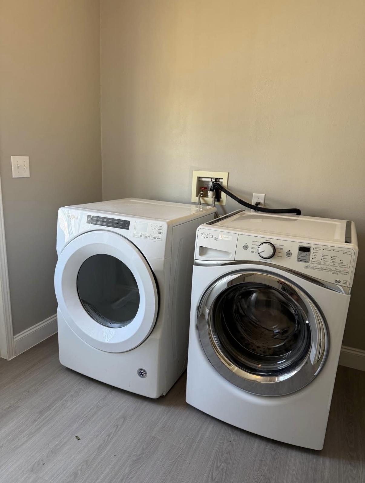 Front-loading washing machine and dryer side by side in a laundry room with light-colored walls and flooring.