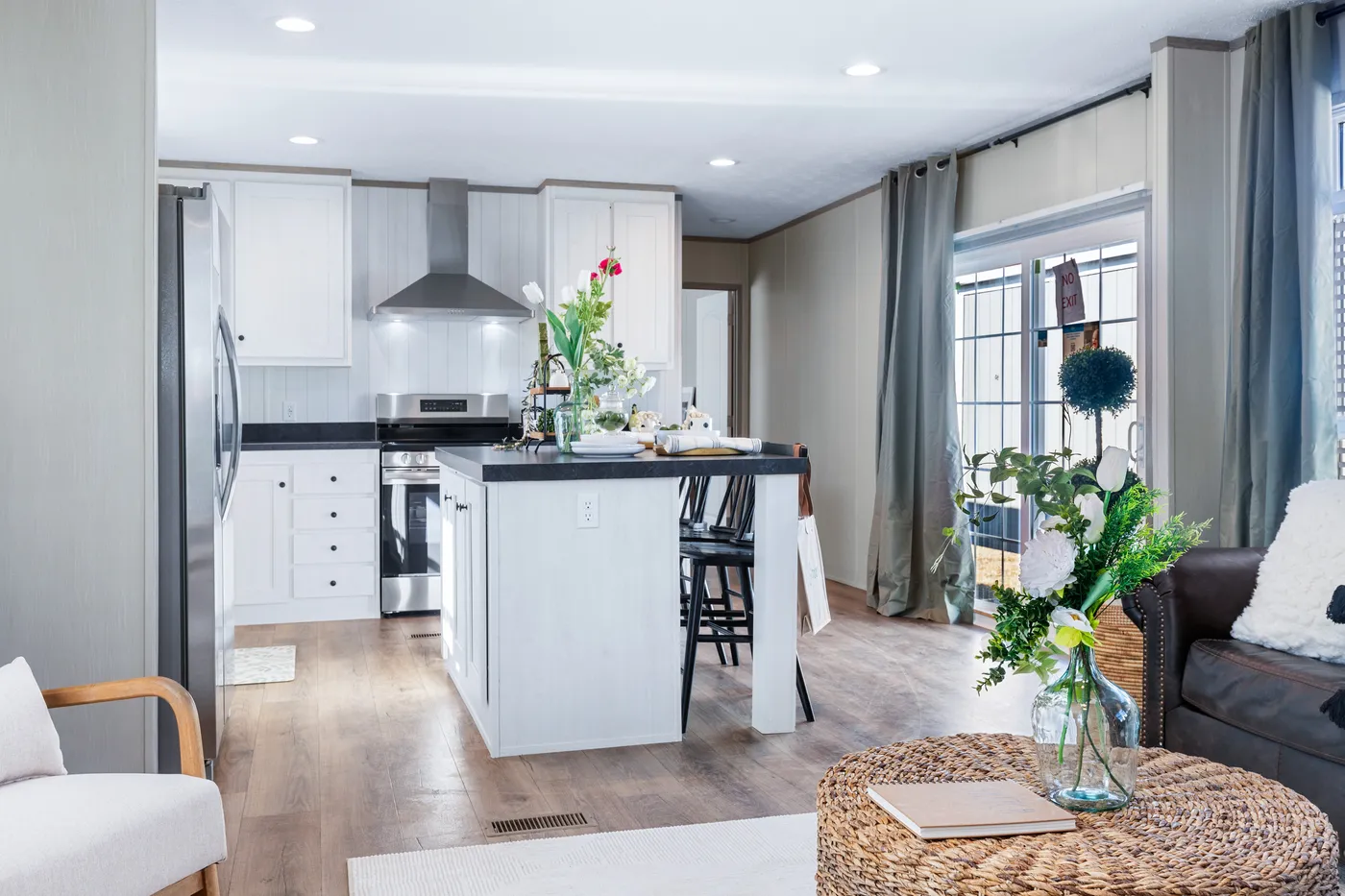 Modern kitchen with white cabinets, stainless steel appliances, and a black island countertop. Dining table and living area with natural light from large windows.